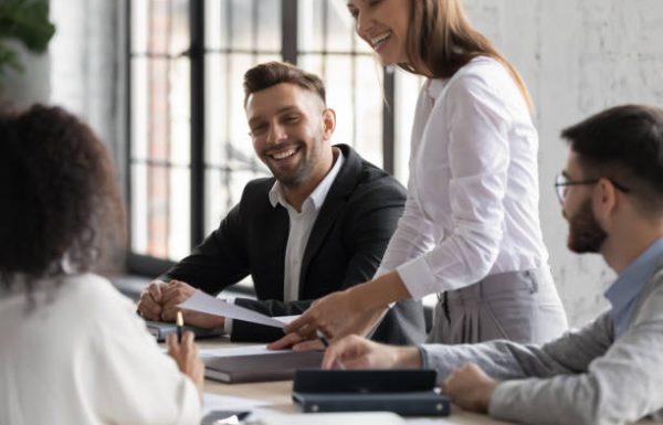 Happy diverse colleagues having fun at corporate meeting, sitting at table in modern boardroom, smiling friendly businesswoman leading briefing, business partners discussing sharing ideas